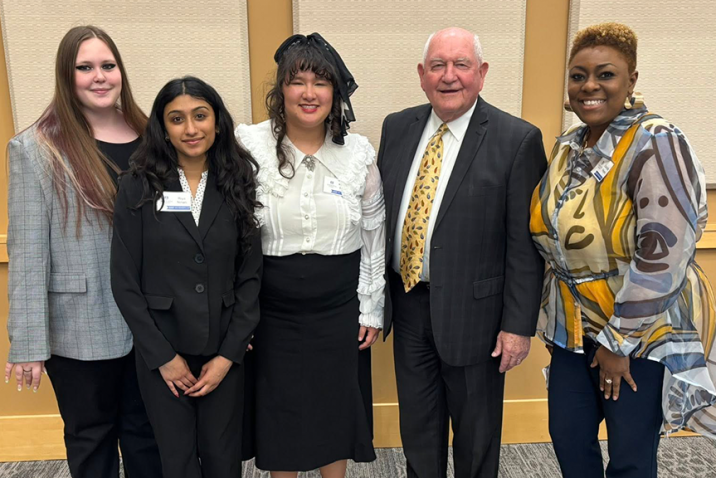 Three college students stand with an older man and a female faculty member.