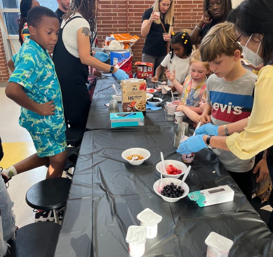 Elementary students standing at a table making fruit and yogurt parfaits.