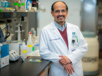 man wearing a scientific lab coat leaning a against counter in a lab