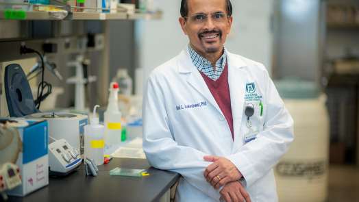 man wearing a scientific lab coat leaning a against counter in a lab
