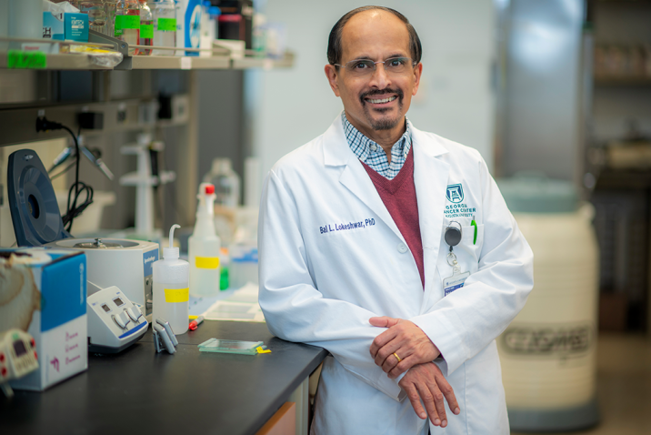 man wearing a scientific lab coat leaning a against counter in a lab