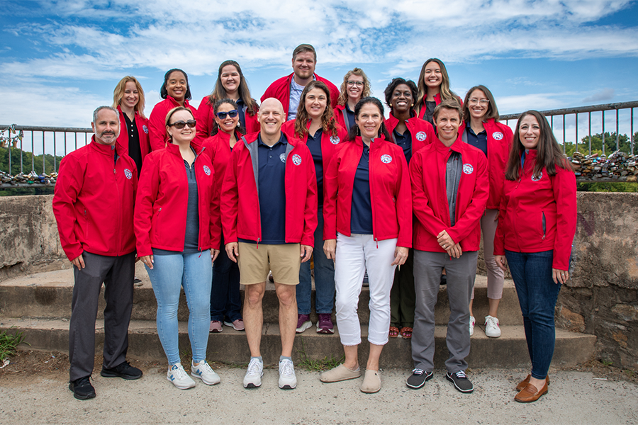 A group of 16 people all wearing red coats stand outside for a group photo.