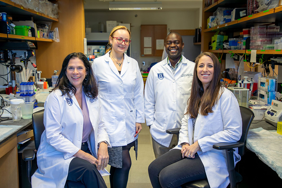 Four scientists, three women and one man, stand in their lab on a college campus.