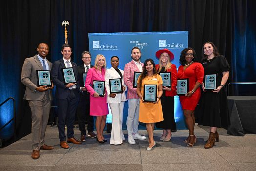 Ten young adults pose on a stage holding a plaque in front of a small banner.