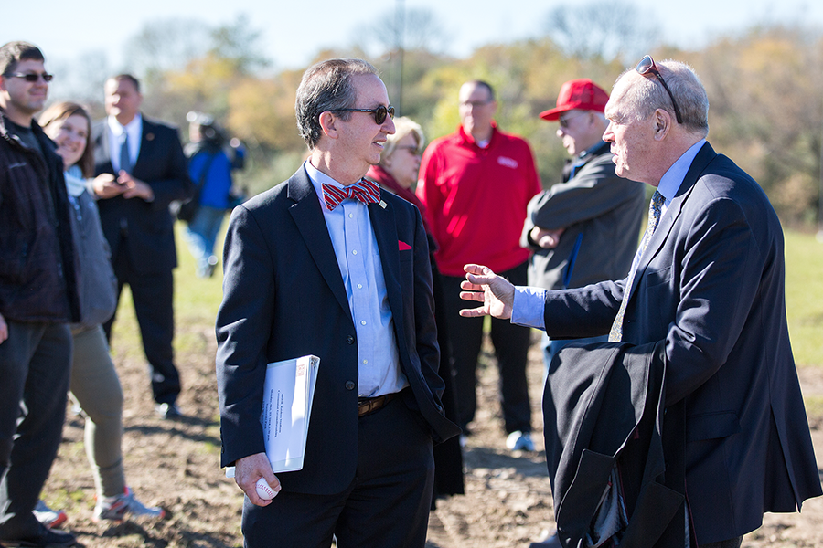 Two men talk following a special ground-breaking ceremony held outside on a college campus.