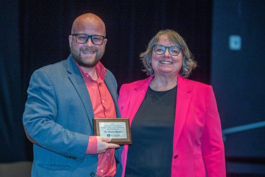 A man holding a small plaque stands next to a woman as both smile for the camera