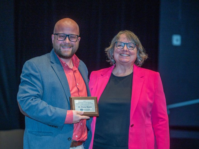 A man holding a small plaque stands next to a woman as both smile for the camera