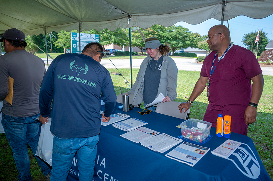 Healthcare workers man a table during a rural health fair as patients review the materials on their table.