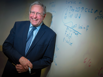 A man stands in front of a dry erase board holding a marker and smiling at the camera.