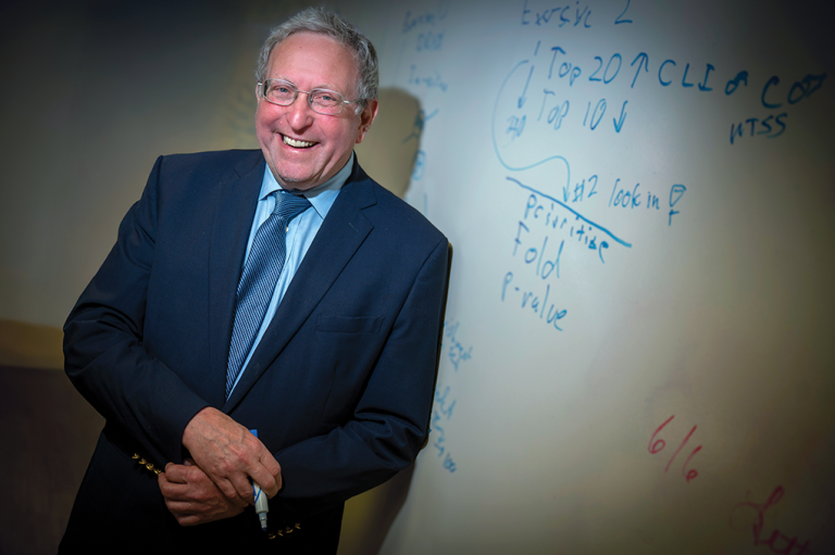 A man stands in front of a dry erase board holding a marker and smiling at the camera.