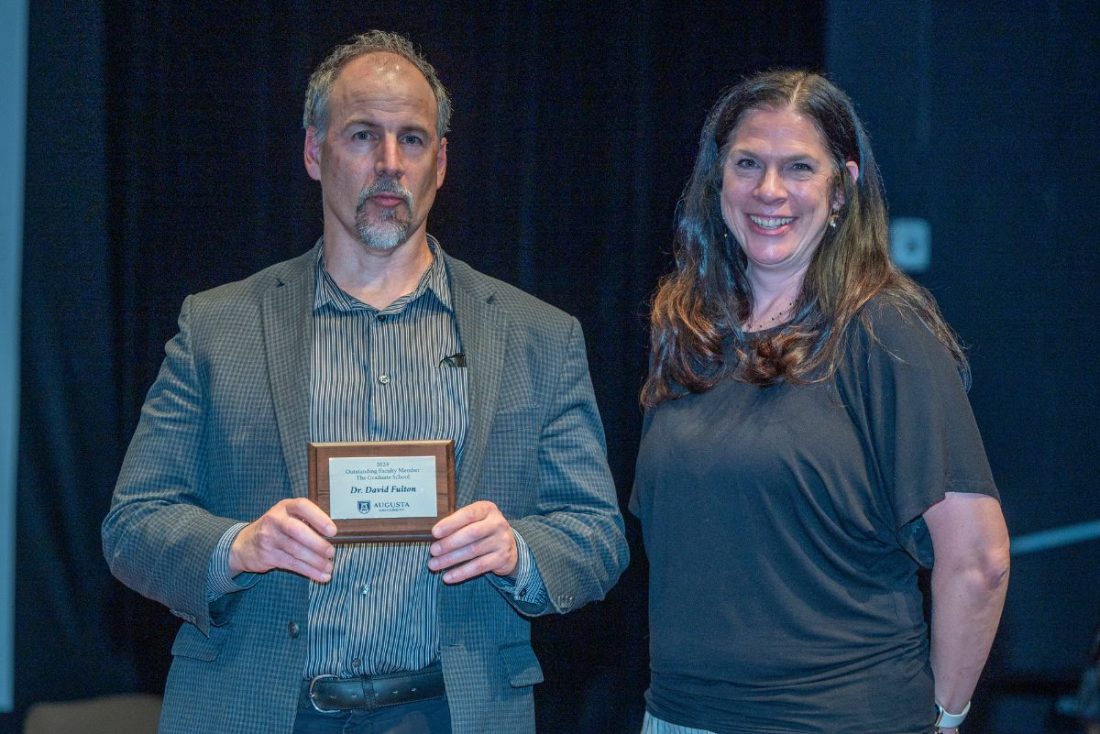 A man holding a small plaque stands next to a woman smiling at the camera.