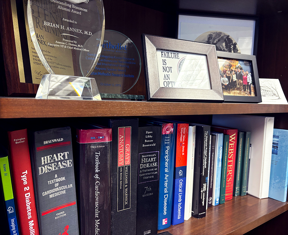 A collection of books related to cardiovascular and heart disease sit on a bookshelf, along with awards presented to Brian H. Annex, MD.