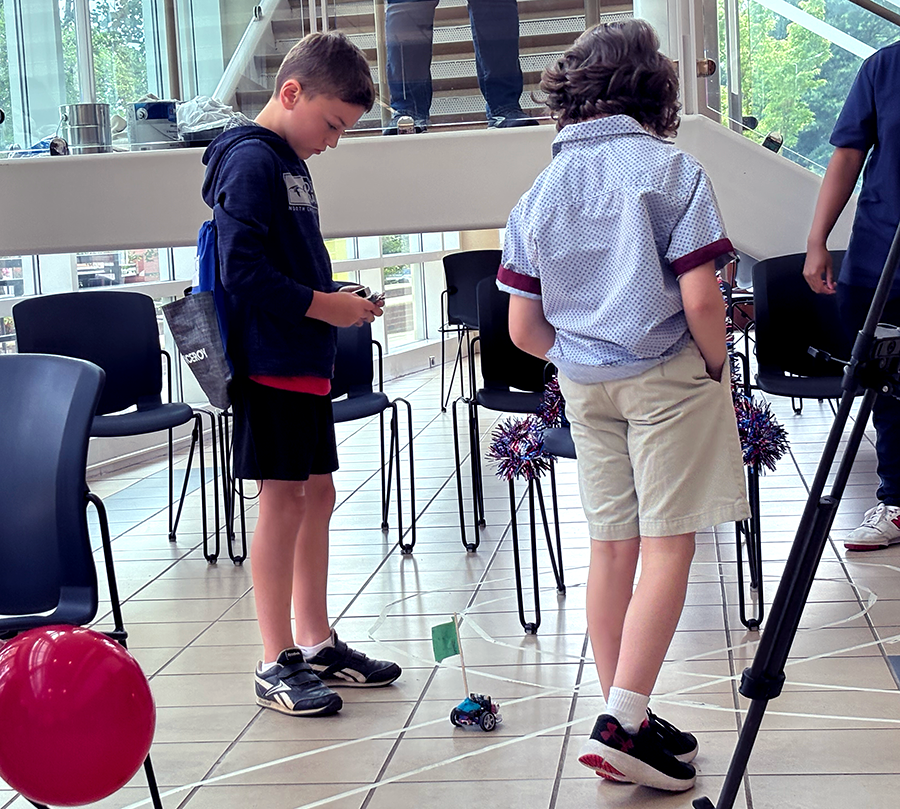Two young boys drive a mini robot car through an obstacle race course.