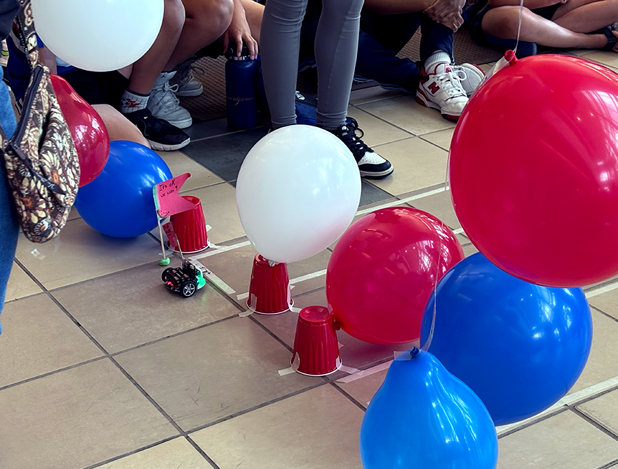 A mini robot car sits at the starting line of a race track. Balloons and solo cups mark the beginning of the course.