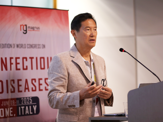 A man stands at a podium with a microphone and delivers a speech in front of a large crowd gathered at an international synposium.