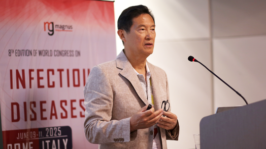 A man stands at a podium with a microphone and delivers a speech in front of a large crowd gathered at an international synposium.