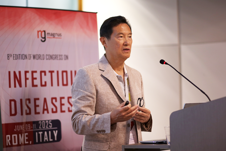 A man stands at a podium with a microphone and delivers a speech in front of a large crowd gathered at an international synposium.