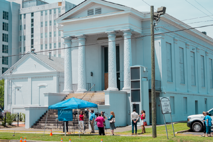 A small crowd gathers near a small blue tent outside a Jewish synagogue to unveil a historical marker.