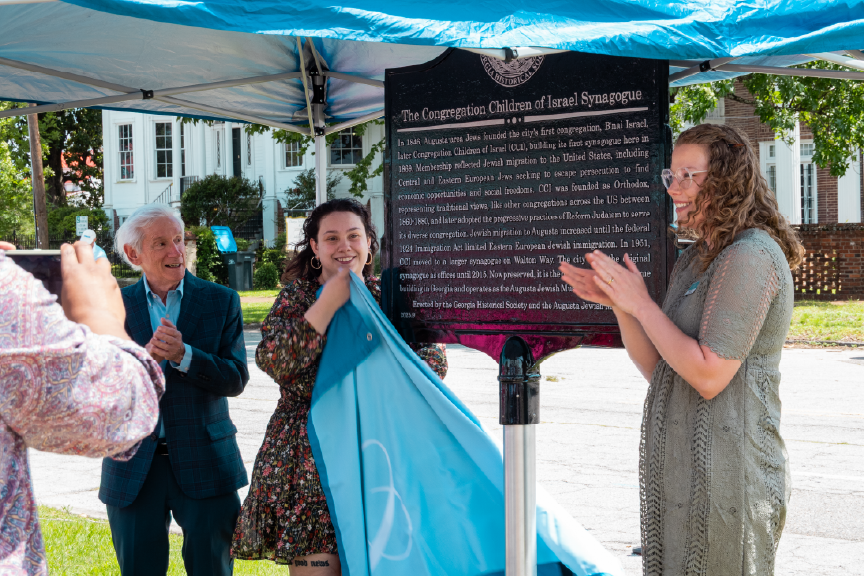 A group of people celebrate the unveiling of a historical marker at an outdoor ceremony.