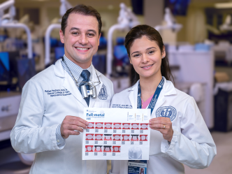 A male dentist and a female dentist wearing lab coats smile and hold up a sheet of paper with instructions on how to prepare a crown printed on it.