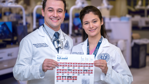 A male dentist and a female dentist wearing lab coats smile and hold up a sheet of paper with instructions on how to prepare a crown printed on it.