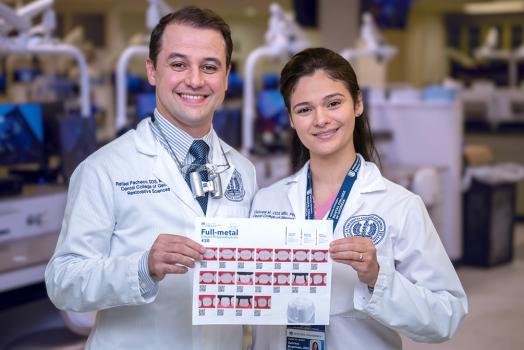 A male dentist and a female dentist wearing lab coats smile and hold up a sheet of paper with instructions on how to prepare a crown printed on it.