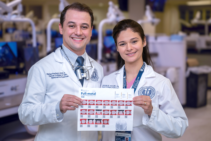 A male dentist and a female dentist wearing lab coats smile and hold up a sheet of paper with instructions on how to prepare a crown printed on it.