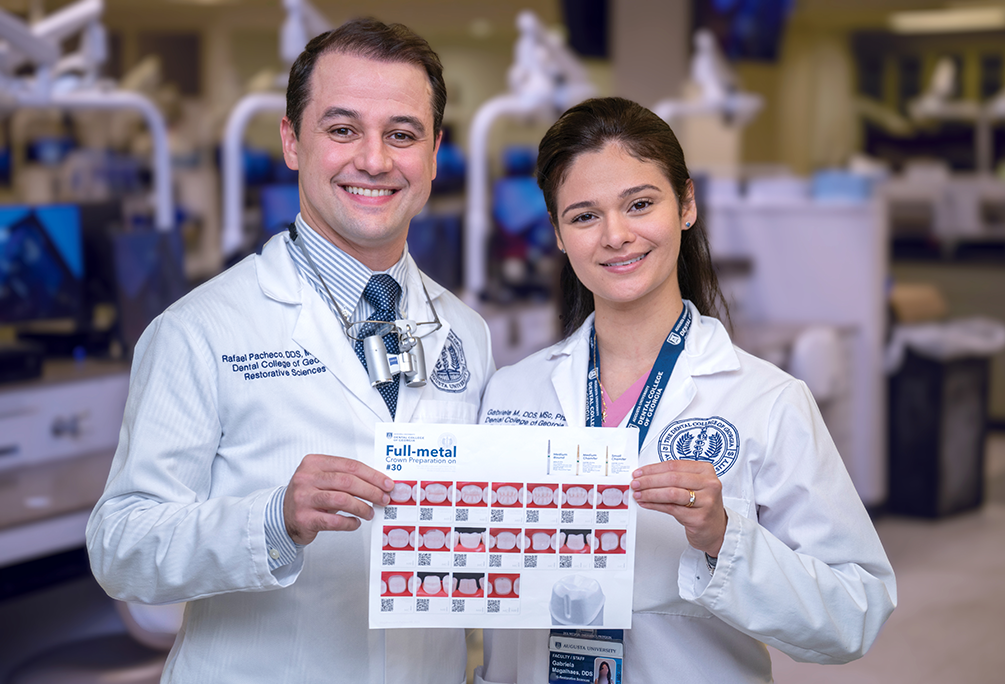 A male dentist and a female dentist wearing lab coats smile and hold up a sheet of paper with instructions on how to prepare a crown printed on it.