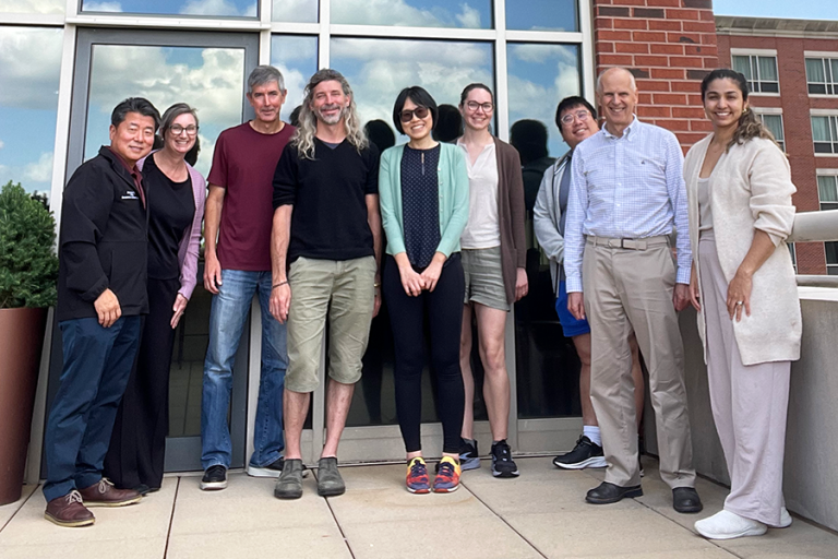 A group of nine people stand outside of a large building.