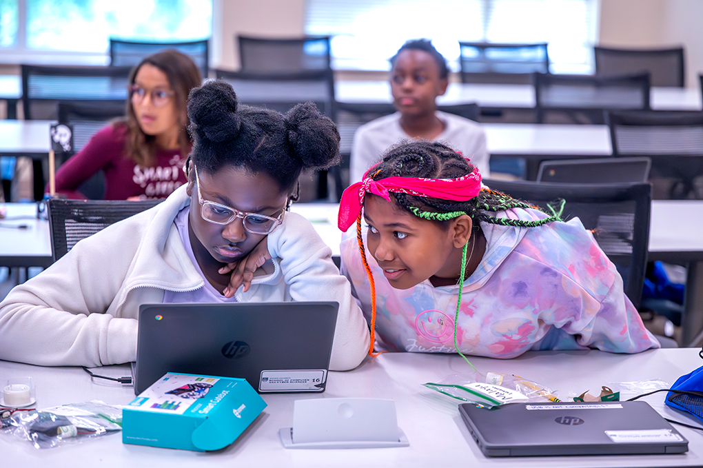 Two young girls use a coding program on a laptop.