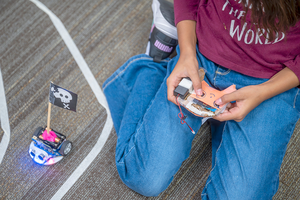 A young girl holds a remote control and operates a miniature vehicle.
