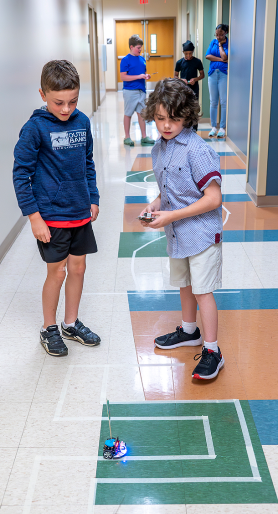 Two young boys operate a remote controlled mini robot car on a race track.