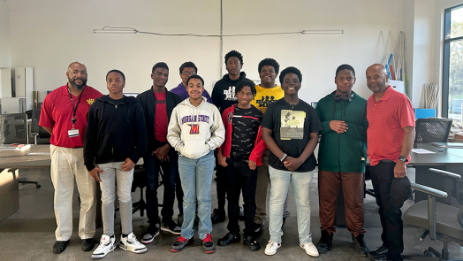 A group of middle and high school students with two counselors stand in a large room.