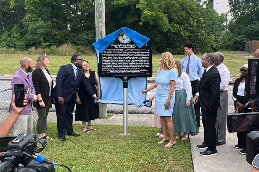 A group of people celebrate as a historical marker is unveiled during an outdoor ceremony.