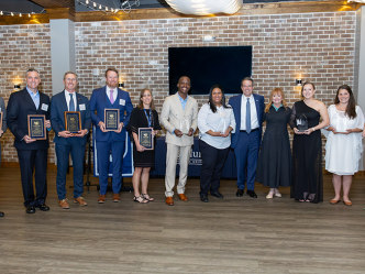 A group of people hold awards and in a large banquet room in front of a larger group of people.