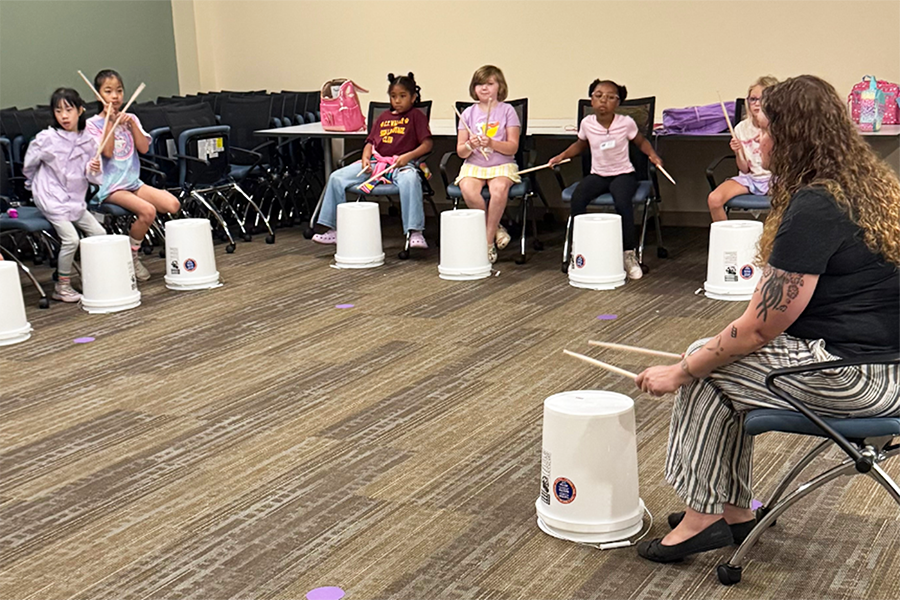 Elementary-aged students learn about rhythm by playing drums on buckets.