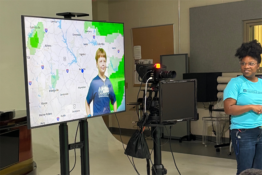 An elementary-aged kid learns about green screen technology used for weather broadcasts during a tour of a news studio.