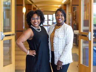 Two women stand in a hallway of a building on a college campus.