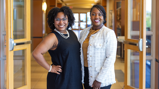Two women stand in a hallway of a building on a college campus.