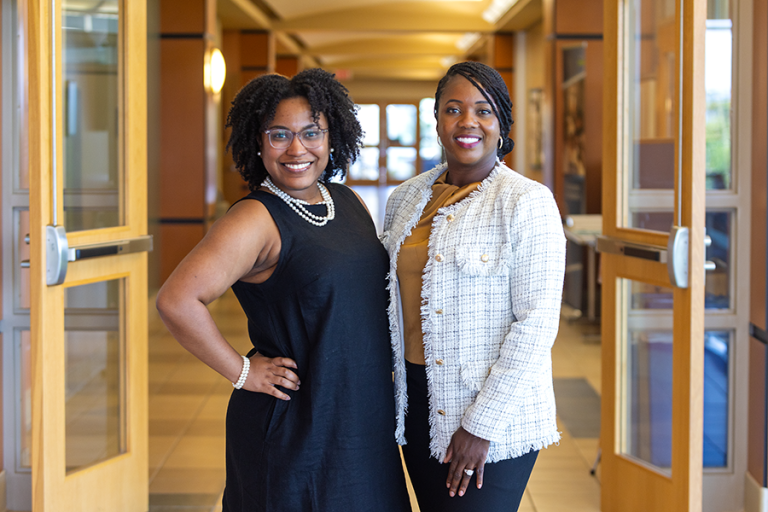 Two women stand in a hallway of a building on a college campus.