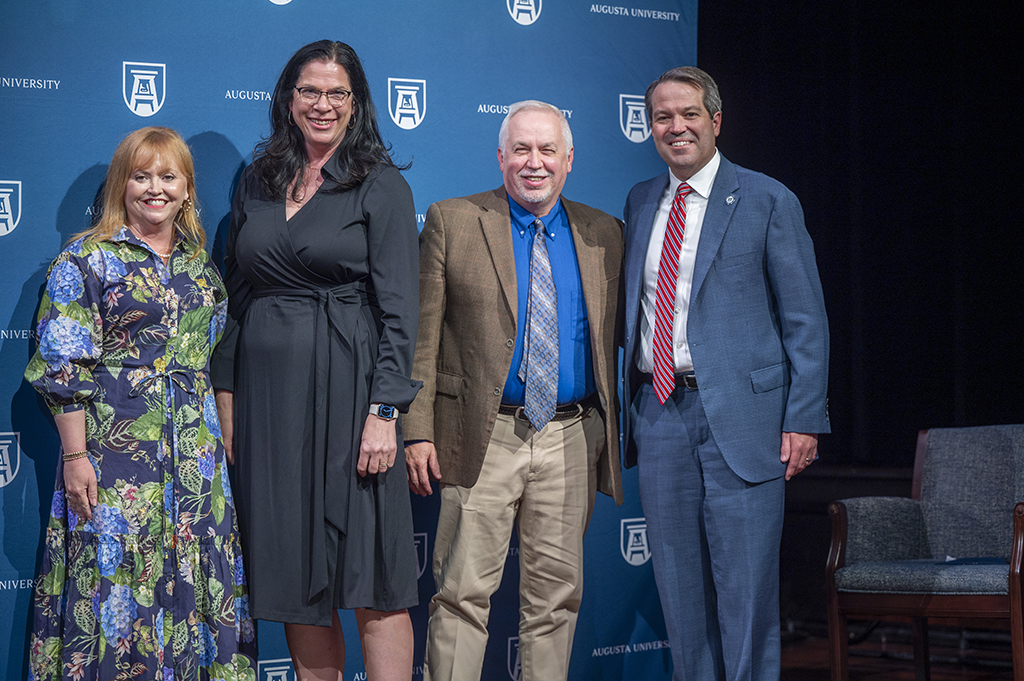 Two women and two men stand together for a photo in front of an Augusta University backdrop