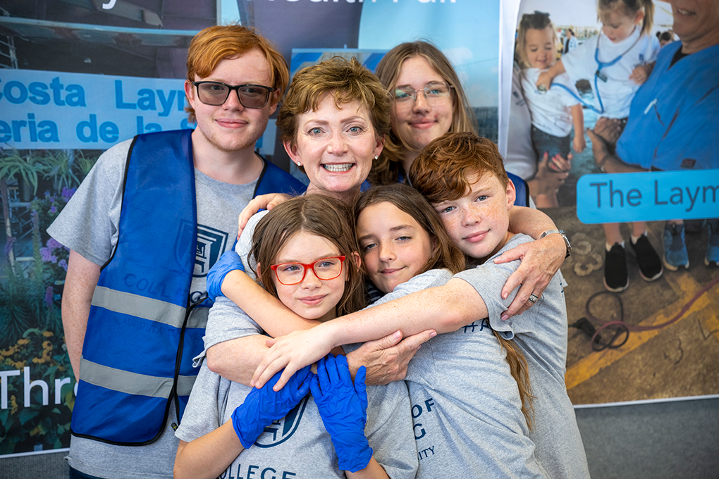 Woman stands smiling with five young children and teens embracing her.