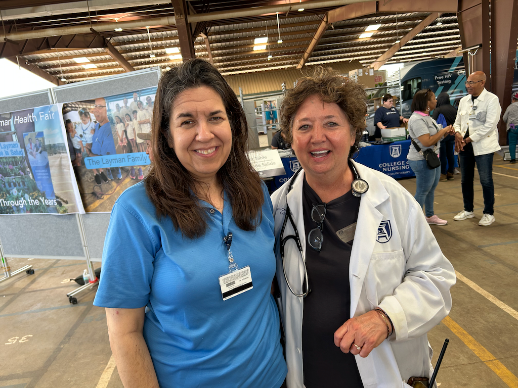Two women smiling, one wearing a lab coat and stethoscope.