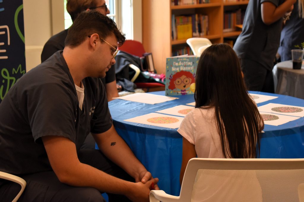 A male college student sits at a table with a young girl, helping her read.