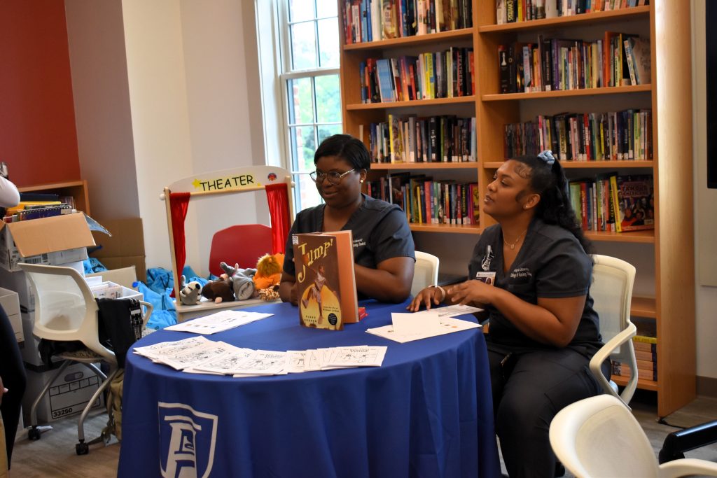 Two college nursing students sit at a table in a modern library. Their table has materials for children that talk about skeletal health.