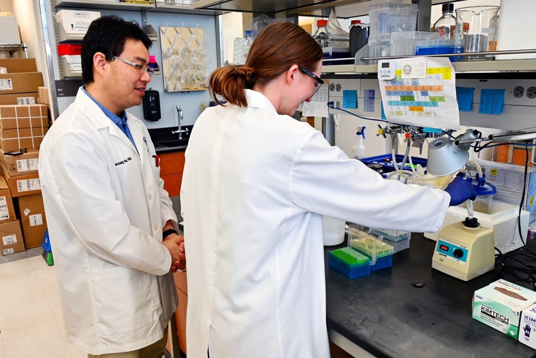 A male scientist and a female high school student work with equipment at a laboratory table.