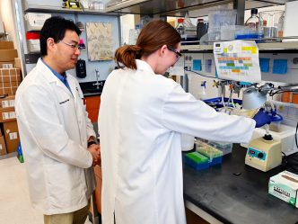 A male scientist and a female high school student work with equipment at a laboratory table.