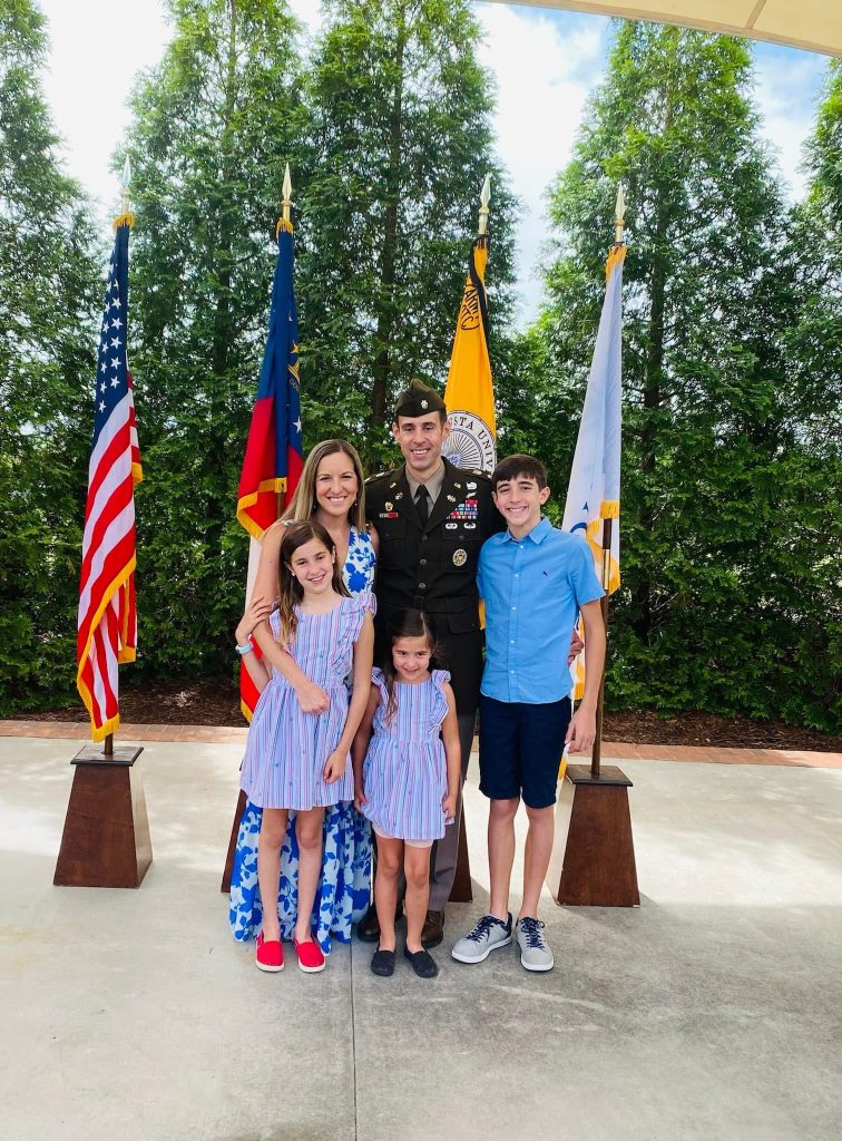 A man and woman with three children stand smiling in front of various flags.