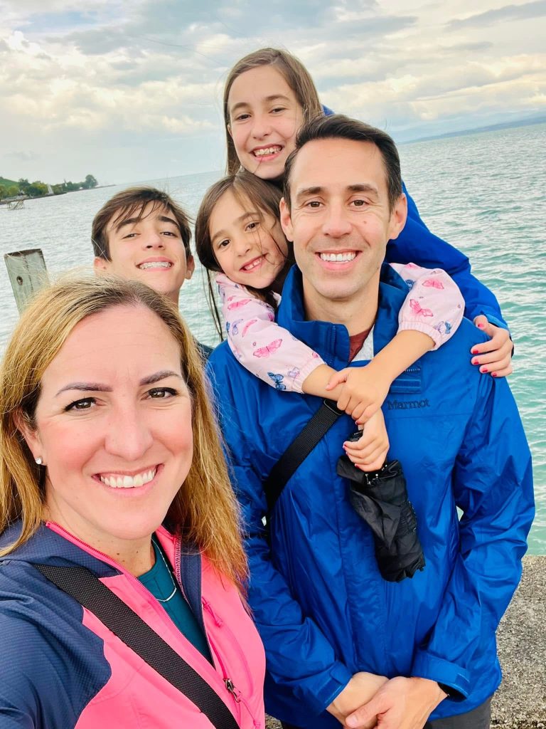 A man and woman with three children smiling in front of water.