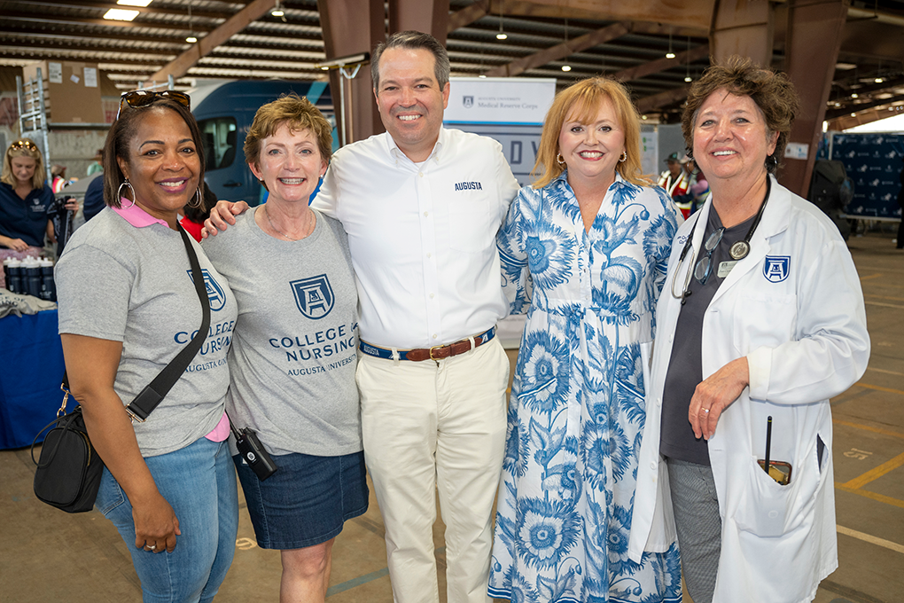 One man stands in the middle of four women smiling with large signs behind them.